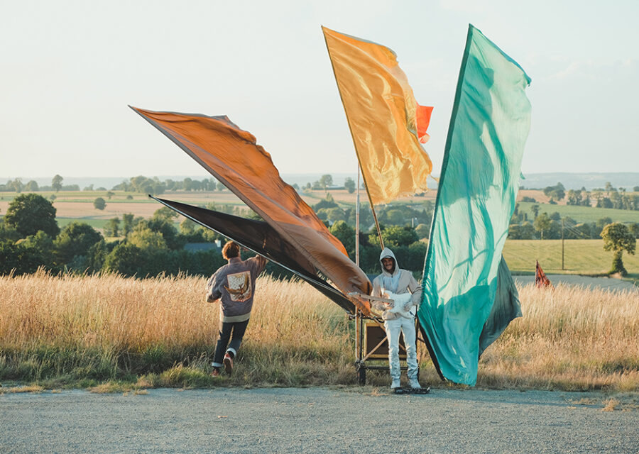 Un comédien dans un champ avec 3 grands drapeaux et un guitariste.